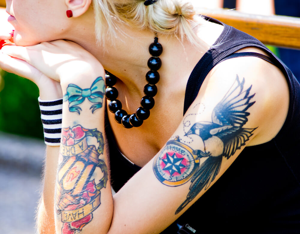 A blonde woman wearing a black tank top with tattoos on her arm